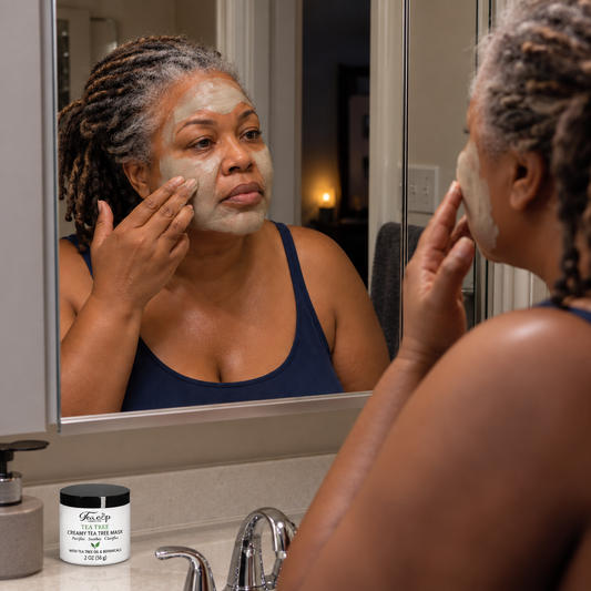 Mature Black woman applying Teacup Cosmetics Creamy Tea Tree Mask at the mirror